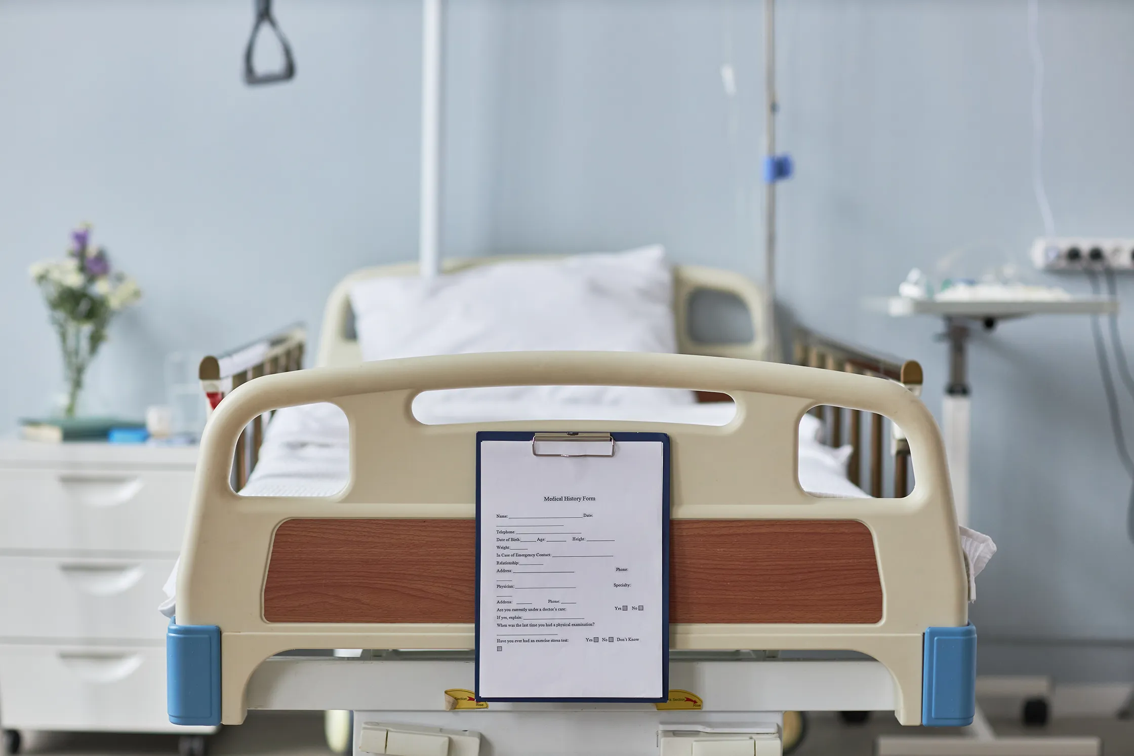 Leeres stationäres Krankenhausbett in Patientenzimmer mit Patientenformular am Fußende. - Deutsch Marketing